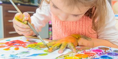 A little girl painting her hand with watercolors. 