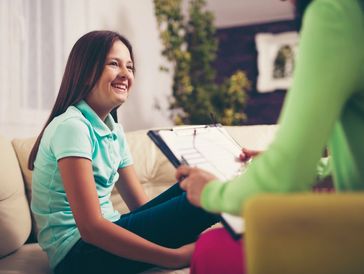 A teenager smiles as another person is asking her information or talking with her nearby. 