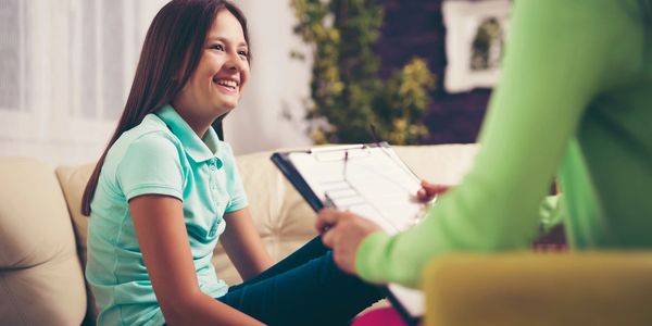 a woman sat on a couch smiling at another person sat opposite holding a clipboard