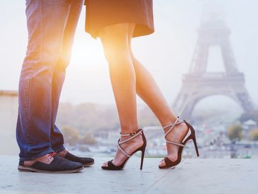 Couple standing close near the Eiffel Tower, sunlit and romantic.