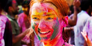 A woman smiling with colorful powder on her face during a vibrant festival.