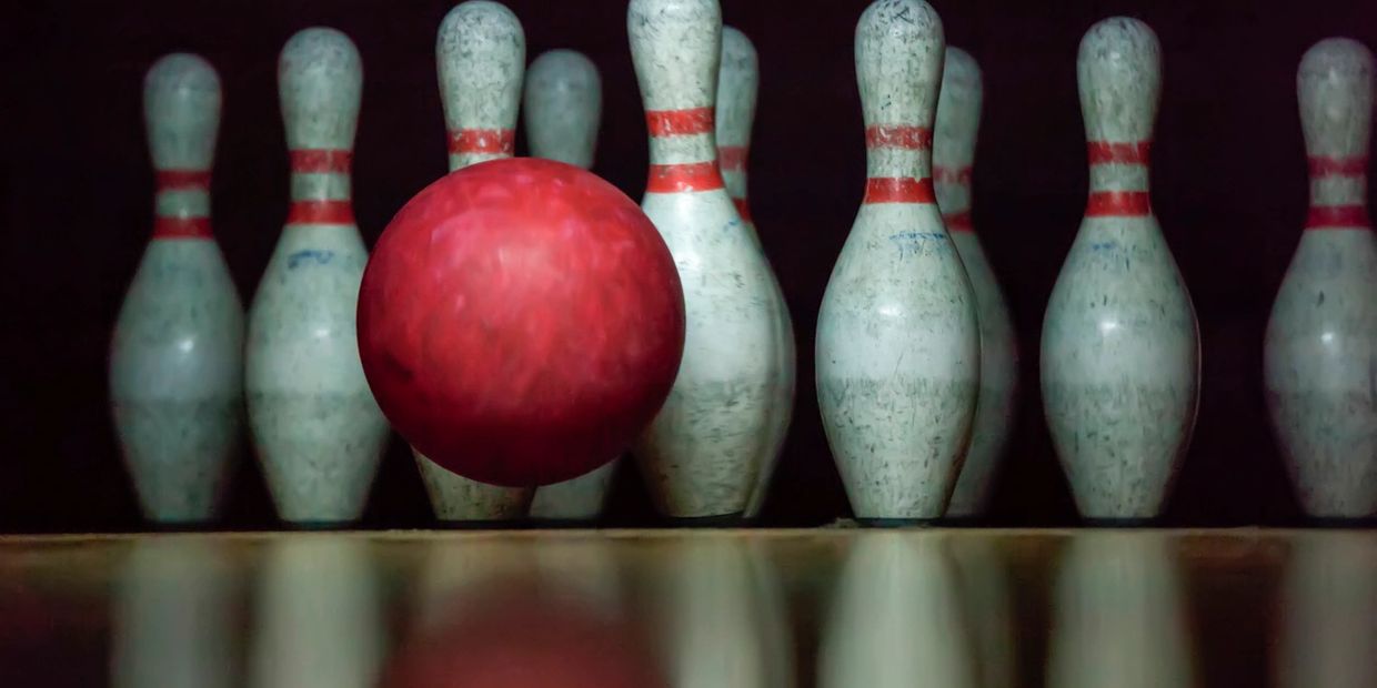 A red bowling ball approaching white pins on a lane.