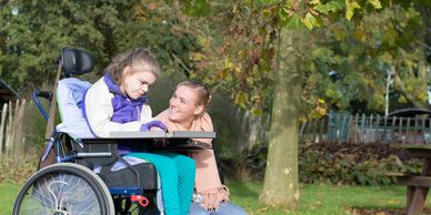 A young woman in a wheelchair with another young woman kneeling next to her. 