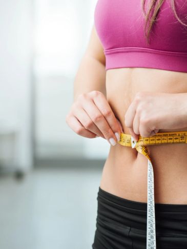 Woman measuring her waist with a tape measure.