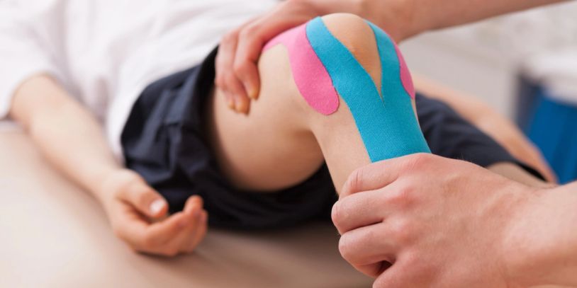 Kinesiology tape applied on a child's knee during therapy.