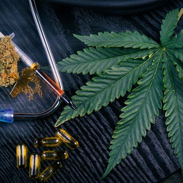 Cannabis leaf with oil capsules and a dab rig on a dark surface.