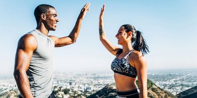 Man and woman athletes raising hands toward each other, smiling, top of hill.