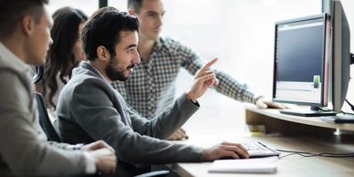 Application Development team of people sitting around a computer working on a project on two screens