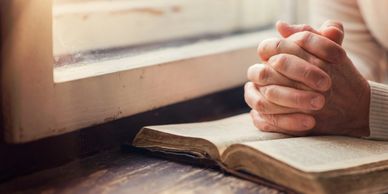 Praying hands on Bible by a window