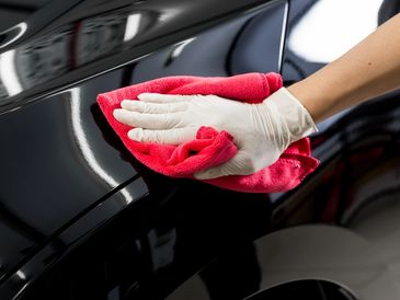 Hand in glove polishing a shiny black car with a red cloth.