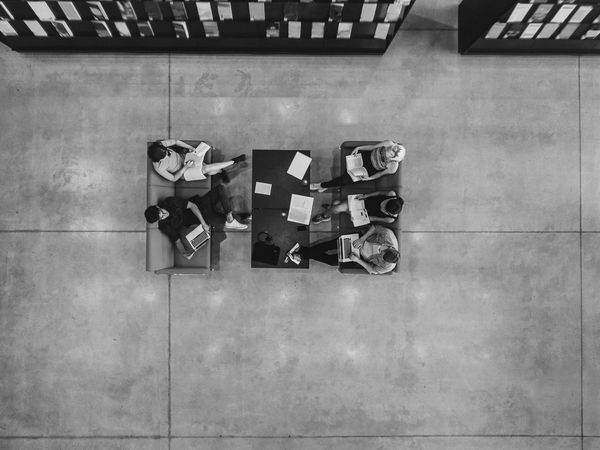 Top view of five people studying and working on laptops and books on orange sofas.