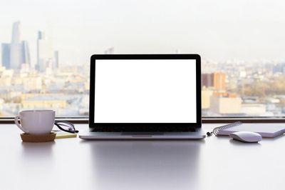 Laptop sitting on a desk overlooking a window with a view of a city.