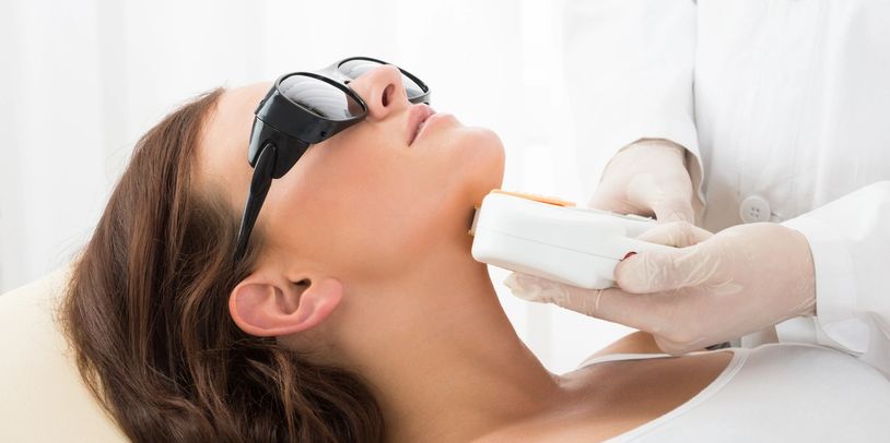 Woman wearing protective glasses receiving laser treatment on her neck.