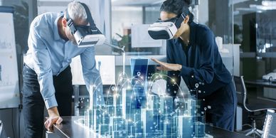 two people wearing vr headsets and looking at a 3d model of a city projected on a tabletop