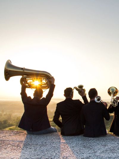 Four musicians with brass instruments at sunset.