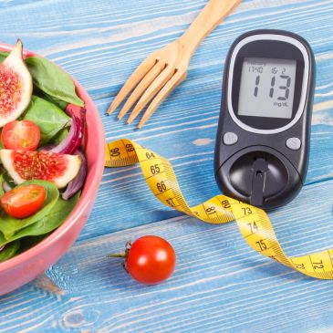 Blood glucose meter, salad bowl, and measuring tape on a wooden table.