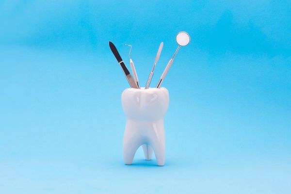 Dental tools arranged in a tooth-shaped holder against a blue background.