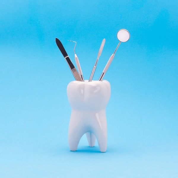 Dental tools in a tooth-shaped holder on a blue background.