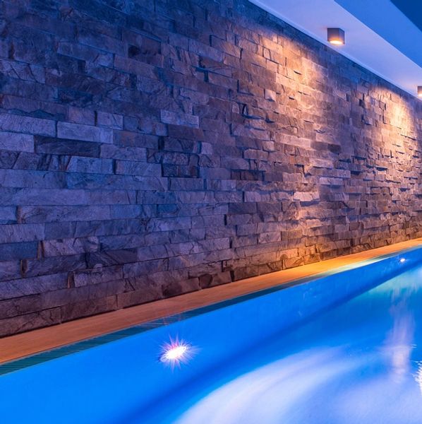 Indoor pool with blue lighting and stone walls.