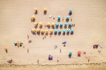 Aerial view of colorful umbrellas and people on a sandy beach.
