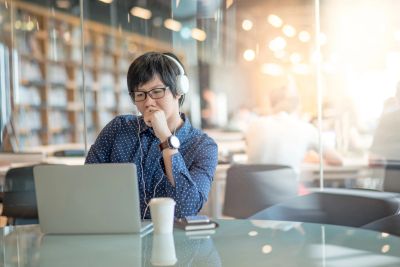 A man wearing headphones working on a laptop in a bright library.