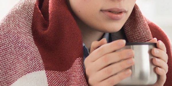 Person wrapped in a blanket holding a metal cup, sipping a warm drink.