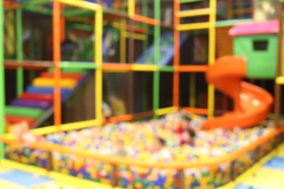 Blurry image of a colorful indoor playground with a ball pit and slide.