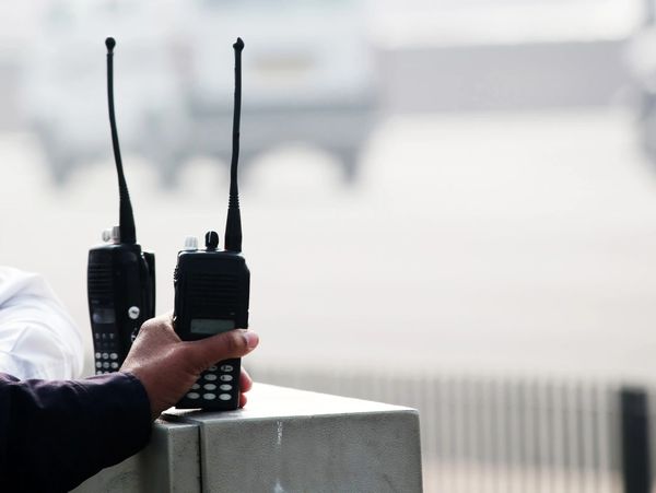 Hand holding a walkie-talkie with two walkie-talkies nearby.