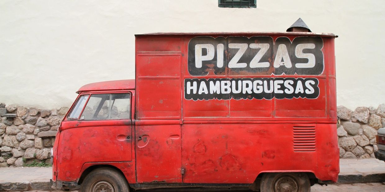 Old red food truck advertising pizzas and hamburgers.