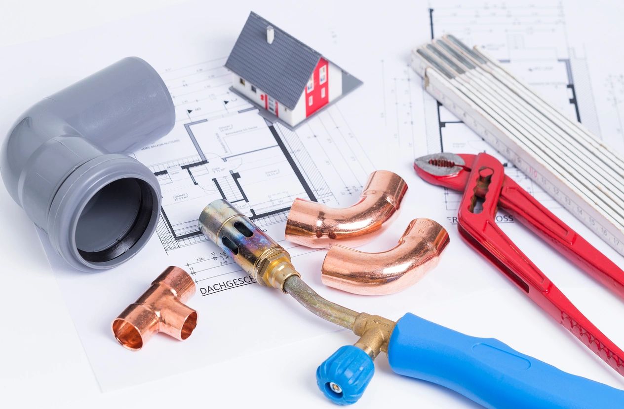 Plumbing tools and pipes arranged on house blueprints with a miniature house model.