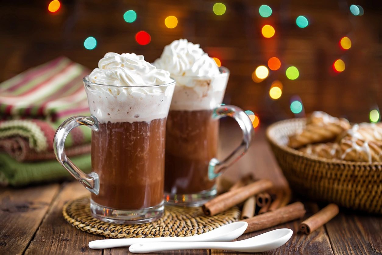 Two mugs of hot chocolate with whipped cream and cinnamon sticks