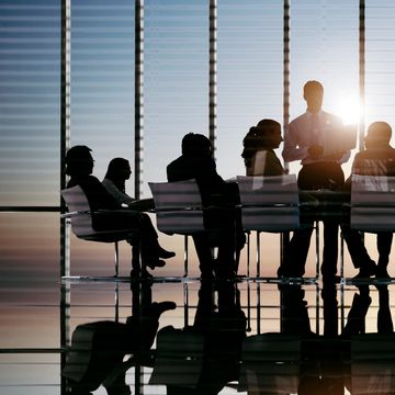Silhouetted business team meeting around a conference table with sunlight streaming through blinds.