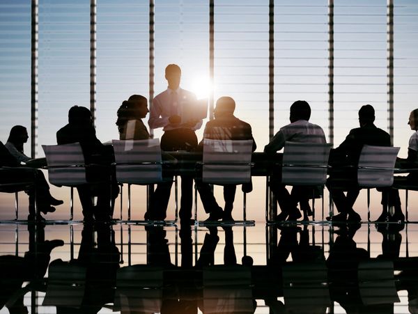 Silhouetted business meeting with presenter in a modern office at sunset.