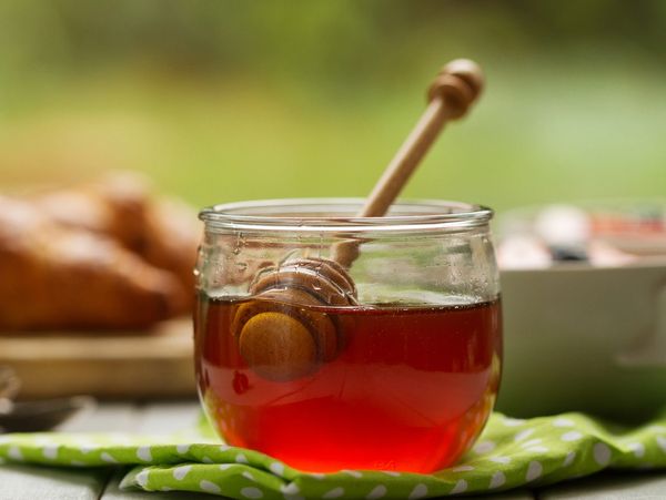A jar of honey with a wooden dipper on a green cloth.