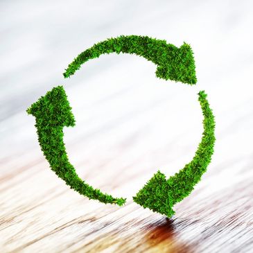 Green recycling symbol made of grass on wooden surface.