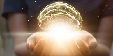 Light emanates from a gold brain down onto a pair of cupped hands.