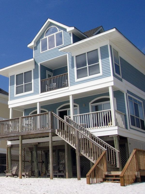 Exterior of blue painted beach house with 3 levels and wooden staircase.