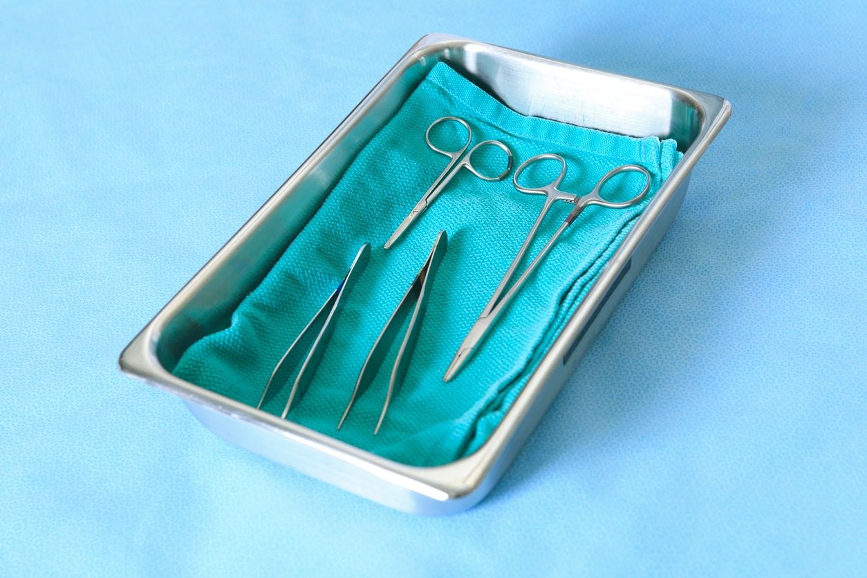 Surgical instruments on a blue cloth in a metal tray.