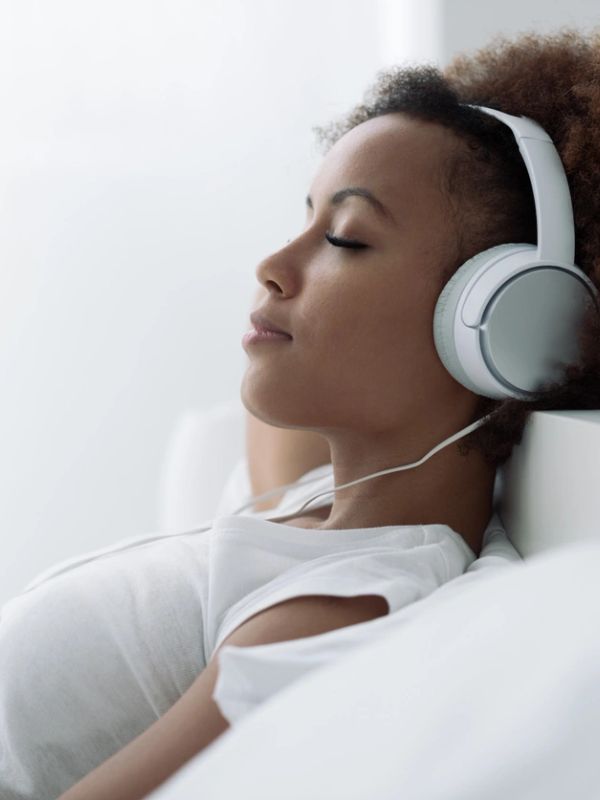 A woman relaxes with eyes closed, listening to music on headphones.
