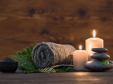 Rolled towel, lit candles, and stacked stones for a calming spa setup.
