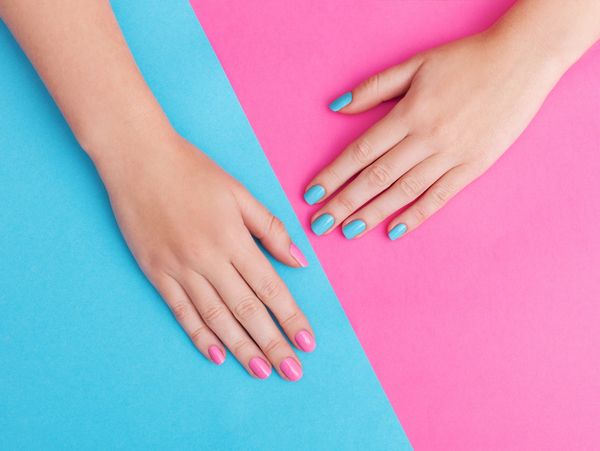 Hands with contrasting pink and blue nail polish on matching split background.
