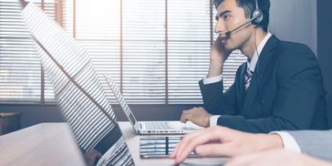 Businessman wearing headset working on laptop in office.