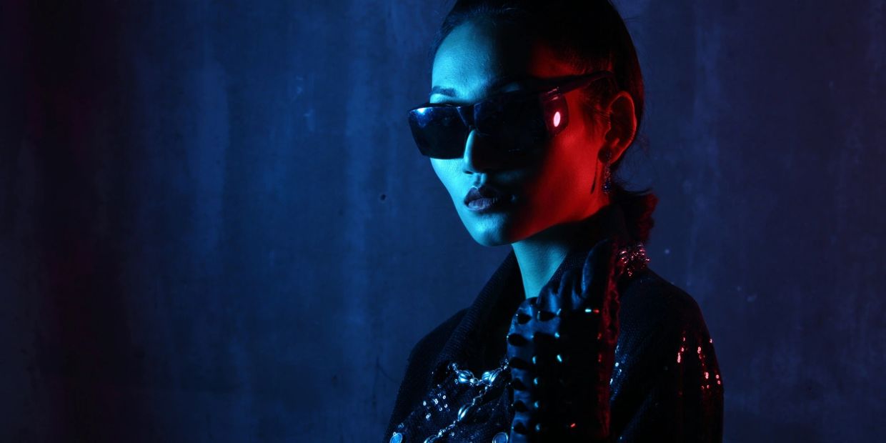 Portrait of a woman in sunglasses with dramatic red and blue lighting.