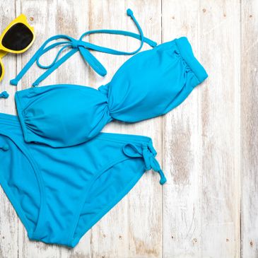 Bright blue bikini with yellow sunglasses on wooden surface.