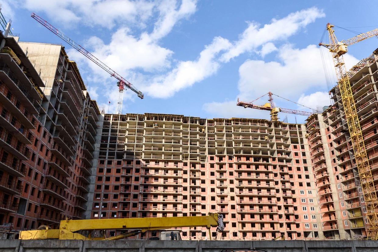 Large residential building under construction with cranes and blue sky.