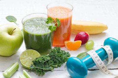 Two healthy smoothies with fresh fruits and a dumbbell wrapped in a measuring tape.