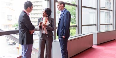 Three professionals having a discussion in an office hallway.