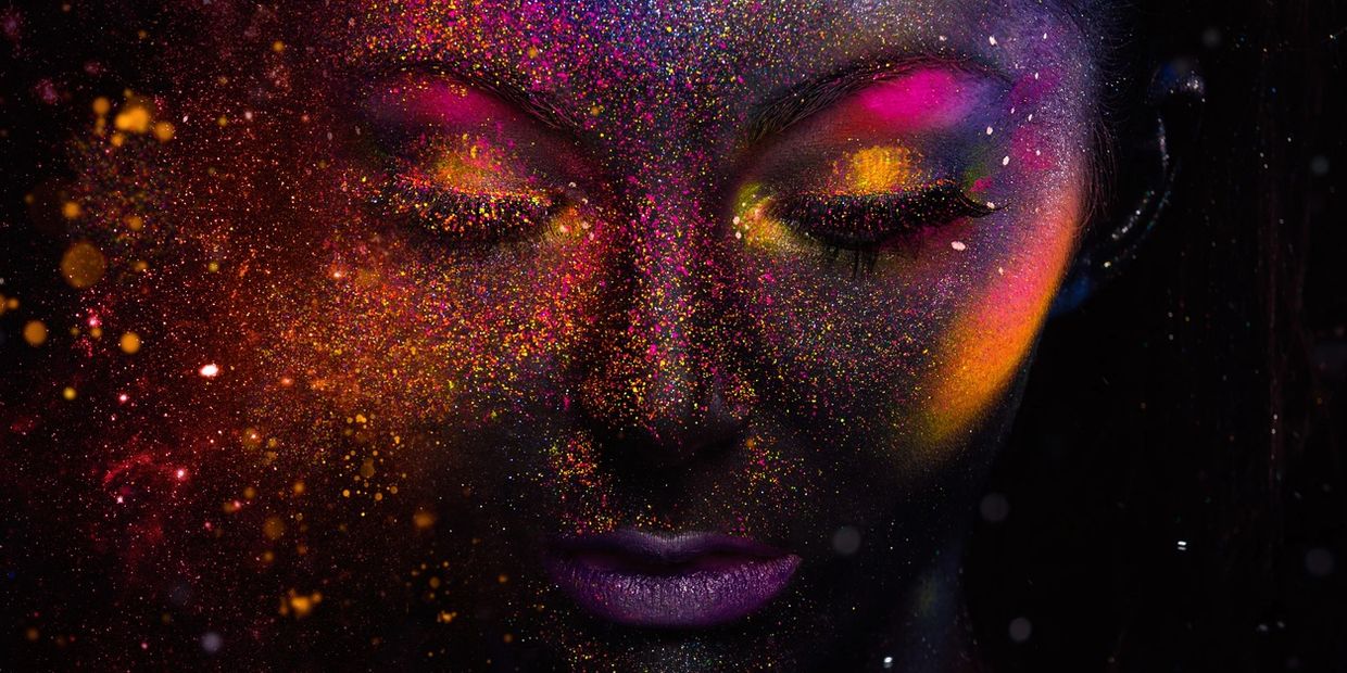 A face covered in vibrant, colorful powder with closed eyes and purple lips.