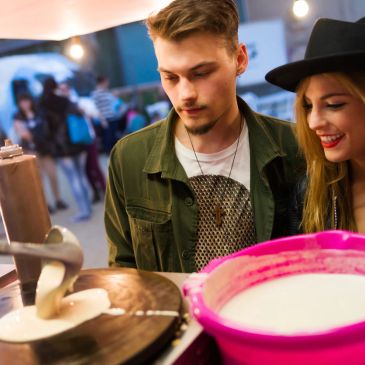 Young man and woman making pancakes at a fair.