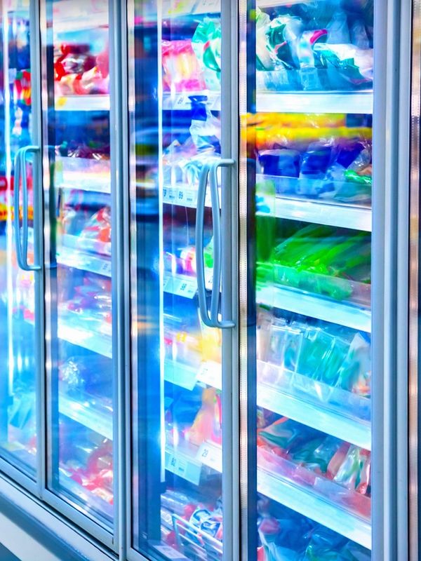 Colorful frozen goods behind glass doors in a grocery freezer aisle.